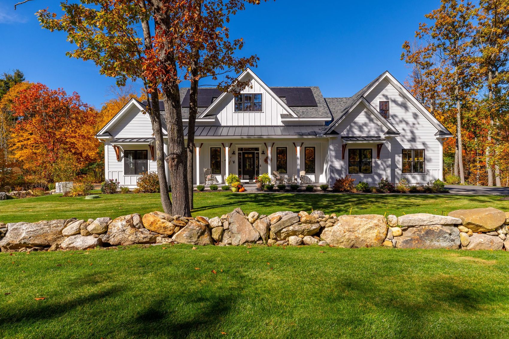 Modern farmhouse with stone walls and fall foliage